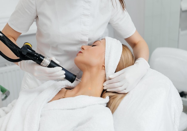 Une jeune fille reçoit un peeling au carbone pour la peau du cou dans un salon de beauté Des impulsions laser nettoient la peau Cosmétologie matérielle Le processus de photothermolyse réchauffe la peau