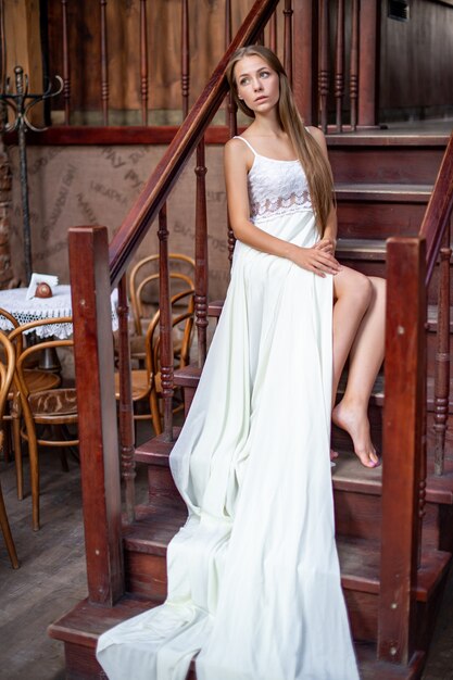 Jeune fille réfléchie en longue robe blanche, assis sur les escaliers