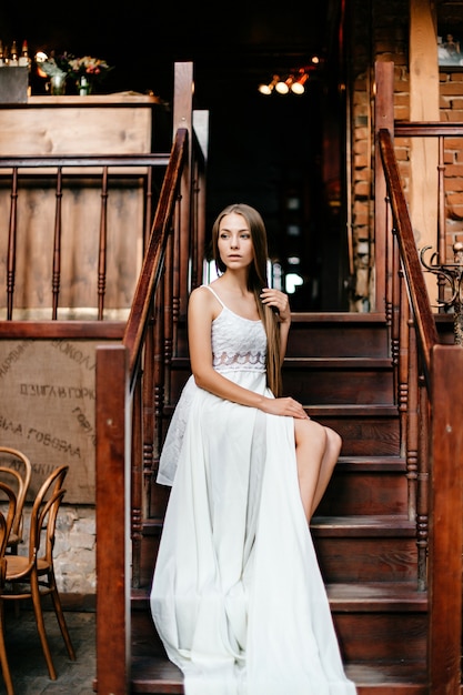 Jeune fille réfléchie romantique en longue robe blanche assise sur les escaliers