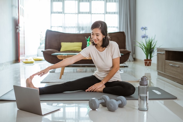 Jeune fille regardant un ordinateur portable et faire des exercices à la maison par elle-même