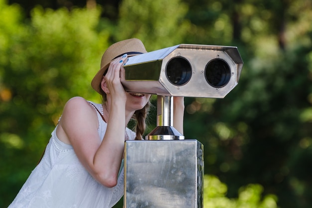 Jeune fille regardant à travers le télescope touristique sur le parc.