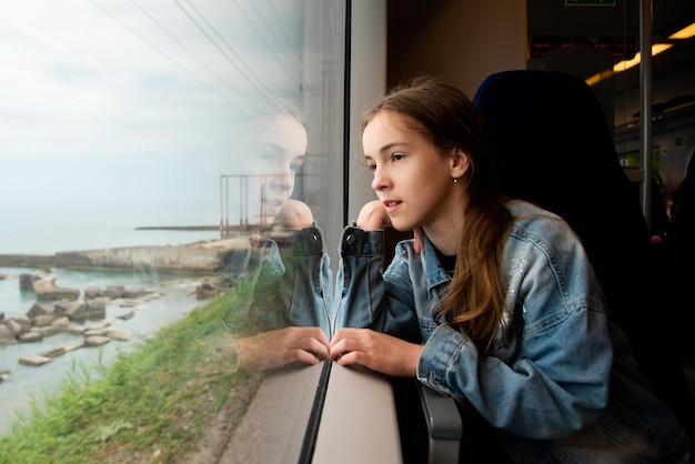 Une jeune fille regarde par la fenêtre d'un train à la mer Voyage Réflexion Vacances Été