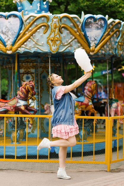 Une jeune fille rit avec du sucre de coton un jour ensoleillé dans un parc d'attractions