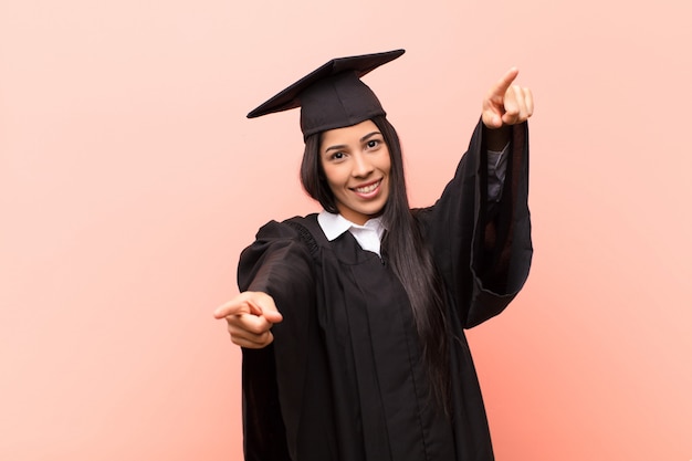 jeune fille en robe de fin d'études se sentant heureux et confiant tout en pointant vers la caméra avec les deux mains