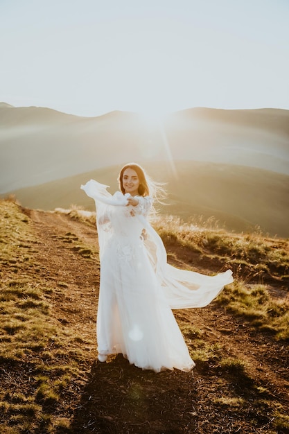 jeune fille en robe de mariée à pied dans les montagnes au lever du soleil le matin