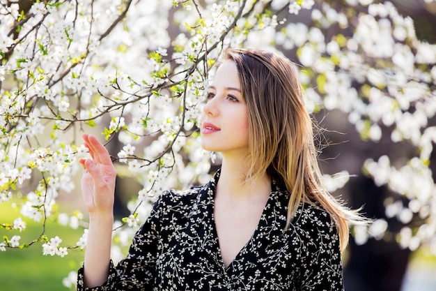 Jeune fille en robe noire reste près d&#39;un arbre en fleurs