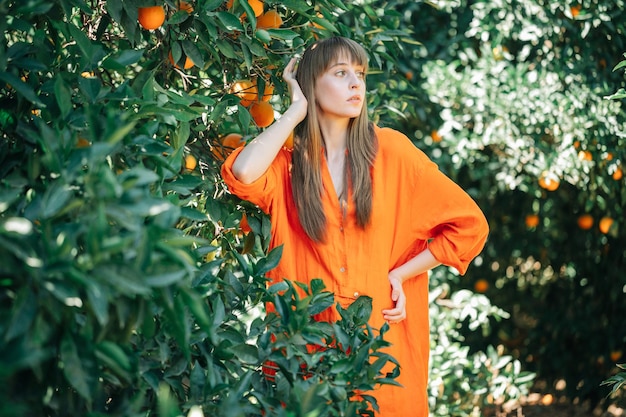 Jeune fille en robe orange regarde à droite en mettant la main gauche derrière la tête dans le jardin orange