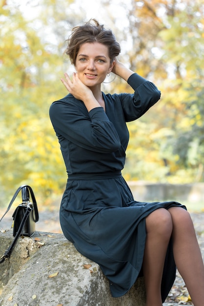 Une jeune fille en robe pose dans un parc sur fond de feuillage d'automne doré.