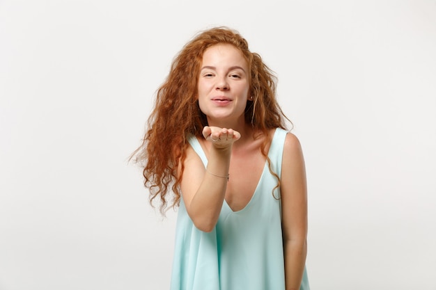 Jeune fille rousse assez souriante dans des vêtements légers décontractés posant isolé sur fond blanc en studio. Concept de mode de vie des émotions sincères des gens. Maquette de l'espace de copie. Soufflant envoyant un baiser aérien.