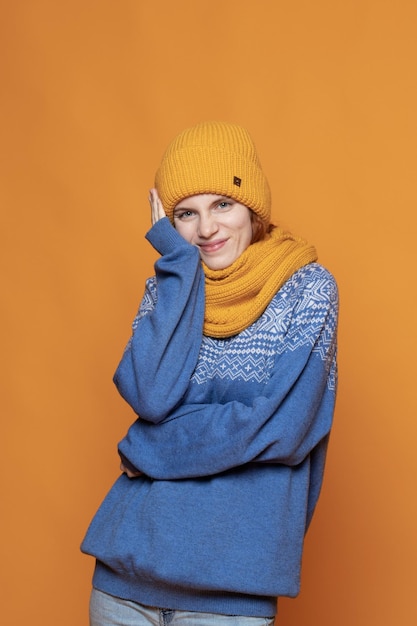 Jeune fille rousse dans un chapeau chaud et un pull en tricot sur fond jaune