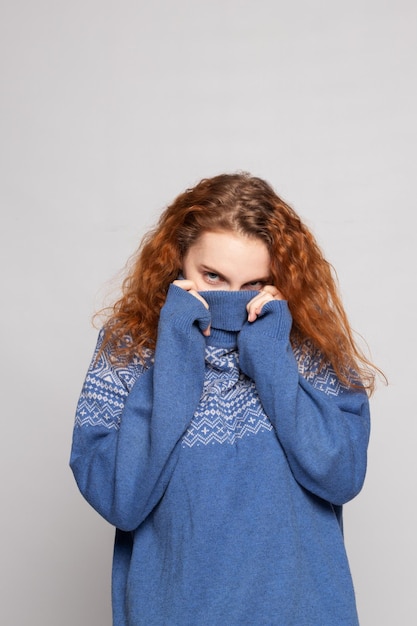 Jeune fille rousse dans un pull en tricot sur fond blanc