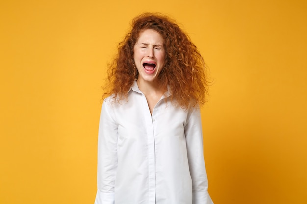 Jeune fille rousse frustrée en chemise blanche posant isolée sur un mur orange jaune