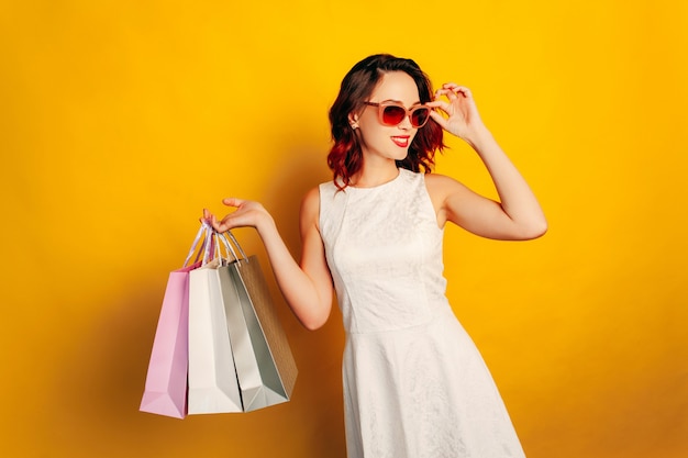 Jeune fille rousse en robe blanche avec des sacs à provisions sur fond jaune