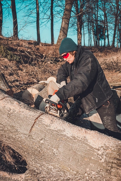 Une jeune fille rurale a coupé une tronçonneuse d'arbre dans des gants pour cuisiner du bois de chauffage pour l'hiver