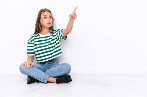 Jeune fille russe assise sur le sol isolé sur fond blanc pointant vers l'extérieur