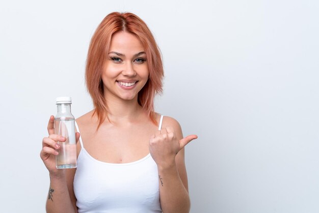 Jeune fille russe avec une bouteille d'eau isolée sur fond blanc pointant vers le côté pour présenter un produit