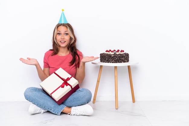 Jeune fille russe célébrant un anniversaire assis sur le sol isolé sur fond blanc avec une expression faciale choquée