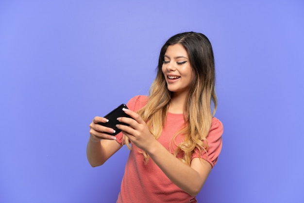 Jeune fille russe isolée sur fond bleu jouant avec le téléphone mobile