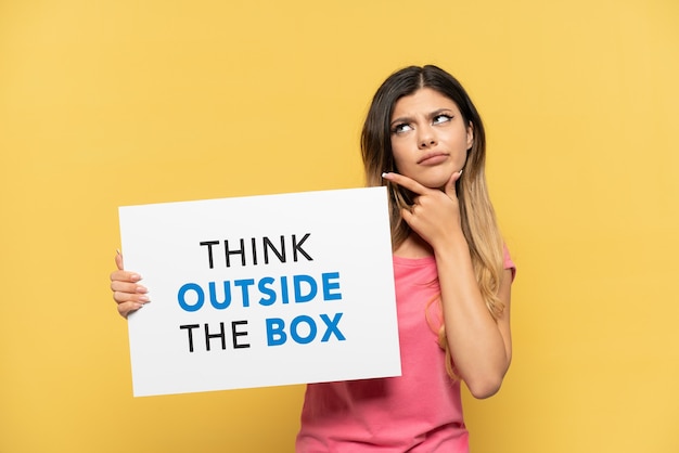 Jeune fille russe isolée sur fond jaune tenant une pancarte avec du texte Think Outside The Box et la pensée