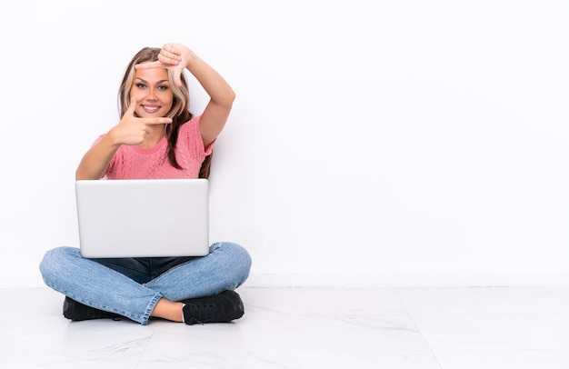 Jeune fille russe avec un ordinateur portable assis sur le sol isolé sur fond blanc se concentrant face symbole de cadrage