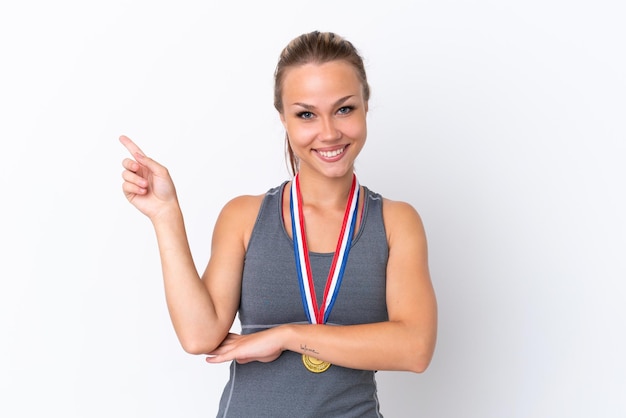 Jeune fille russe sportive avec des médailles isolées sur fond blanc, pointant le doigt sur le côté