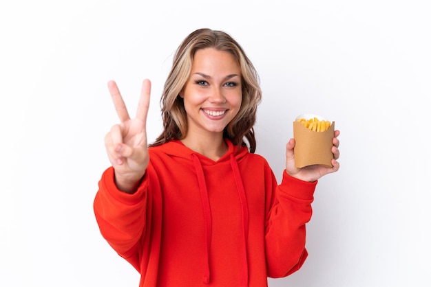 Jeune fille russe tenant des chips frites isolées sur fond blanc souriant et montrant le signe de la victoire