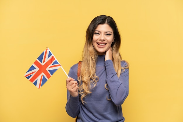 Jeune fille russe tenant un drapeau du Royaume-Uni isolé sur fond jaune en riant