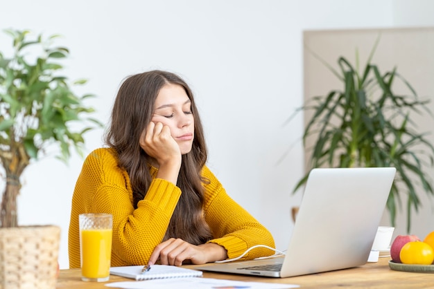 La jeune fille s'est endormie devant un ordinateur portable. La femme mignonne s'ennuie, est fatiguée ou surmenée.