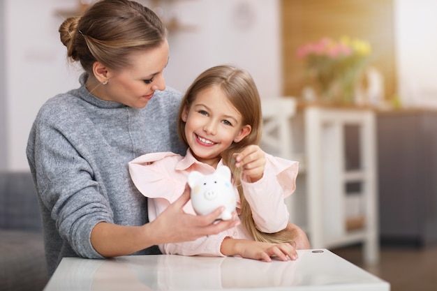 Jeune fille et sa mère avec tirelire assis à table