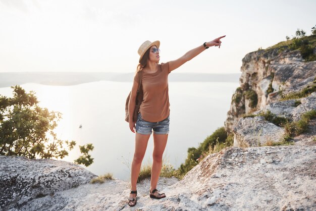 Jeune fille avec sac à dos, profitant du coucher de soleil au sommet de la montagne rocheuse Concept de vacances aventure voyage lifestyle