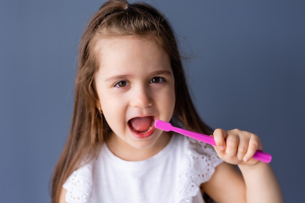 Une jeune fille se brosse les dents avec une brosse à dents rose.