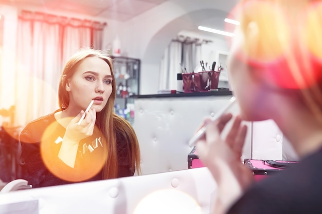 Une jeune fille se maquille dans un salon de beauté. La fille devant le miroir se maquille. Salon de beauté