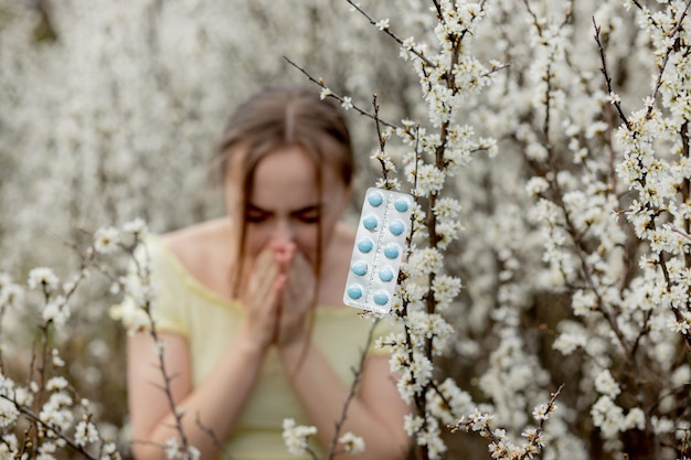 Photo jeune fille se moucher et éternuer dans les tissus devant l'arbre en fleurs. allergènes saisonniers affectant les personnes. belle dame a une rhinite.