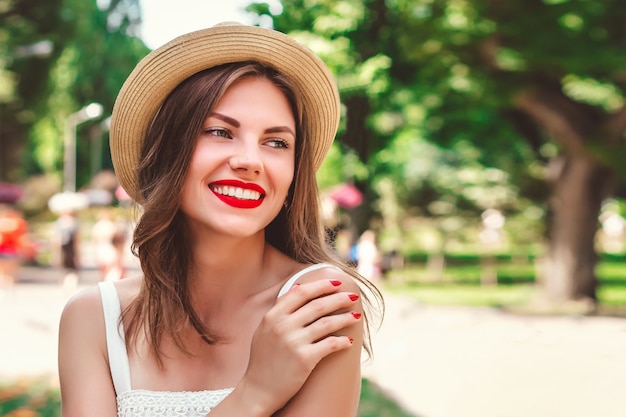 Une jeune fille se promène dans le parc et sourit. Portrait d'une jeune femme au chapeau de paille avec rouge à lèvres rouge