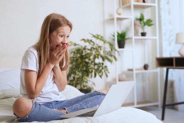 La jeune fille se réjouit du message en ligne sur l'ordinateur portable