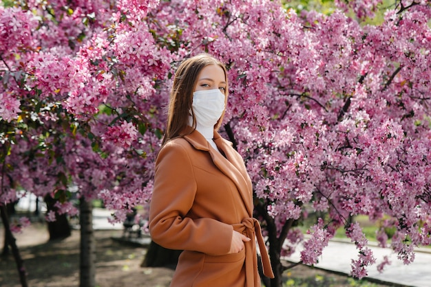 Une jeune fille se tient dans un jardin fleuri portant un masque contre les allergies et les pandémies. Allergie aux fleurs.