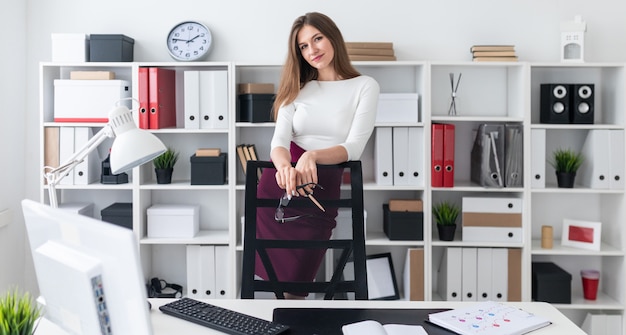 Une jeune fille se tient près de la table et pose ses mains sur le dossier d'une chaise haute.