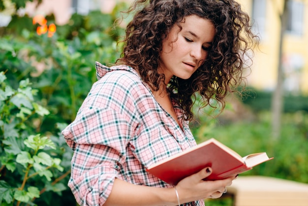 Une jeune fille séduisante dans le parc lit avec fascination un livre intéressant