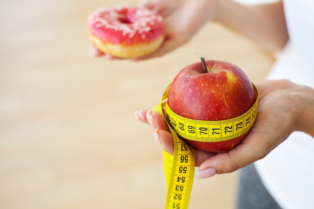 Une jeune fille séduisante fait le choix entre des aliments sains et nocifs tenant une pomme et un hamburger dans ses mains.