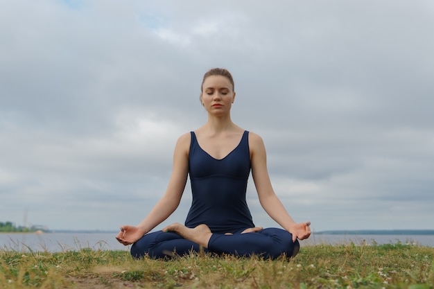 Jeune fille séduisante pratiquant le yoga, assise dans l'exercice Half Lotus, pose d'Ardha Padmasana. Formation de yogi, méditation en plein air, mode de vie sain