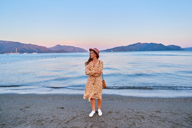 Une jeune fille sereine et calme, une voyageuse pensive portant un chapeau et une robe, est seule et regarde au loin en été