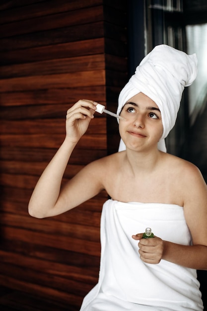 Jeune fille avec une serviette sur la tête fait des soins du visage Soins de la peau hydratants avec du sérum