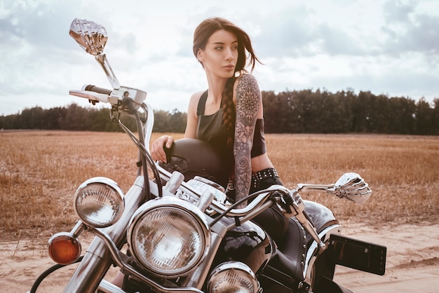 Jeune fille sexy posant sur une moto au coucher du soleil. Concept de sport automobile. Technique mixte