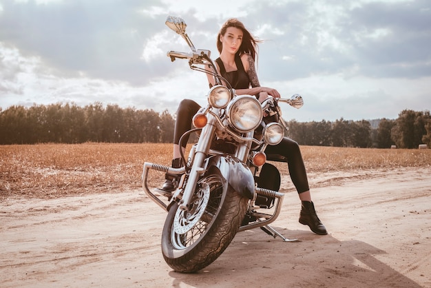 Jeune fille sexy posant sur une moto au coucher du soleil. Concept de sport automobile. Technique mixte