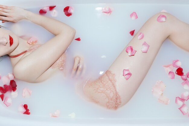 Jeune fille sexy prenant un bain de lait avec des pétales de rose