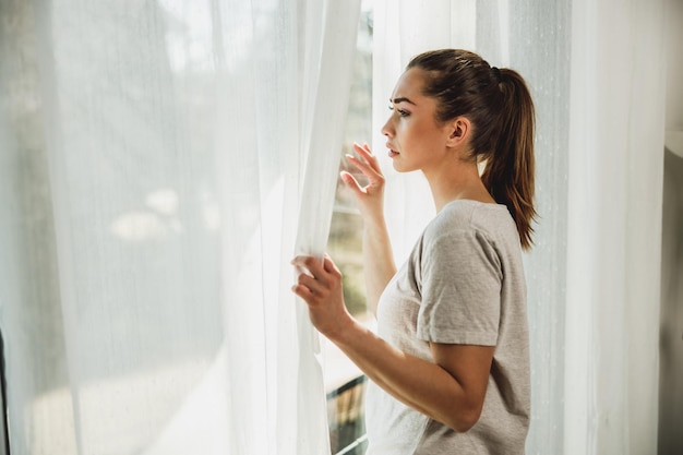 Jeune fille solitaire en dépression regardant par la fenêtre perdue dans de mauvaises pensées pessimistes.