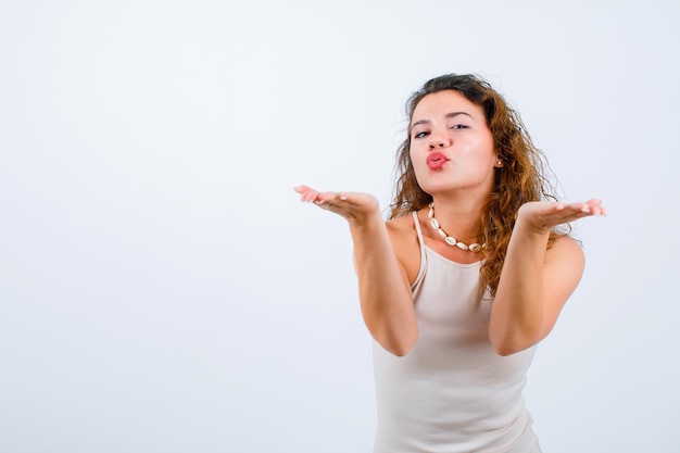 La jeune fille souffle le baiser à l'appareil-photo sur le fond blanc