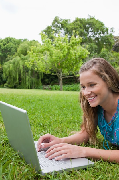 Jeune fille souriante à l&#39;aide de son ordinateur portable dans un parc en position couchée sur l&#39;herbe