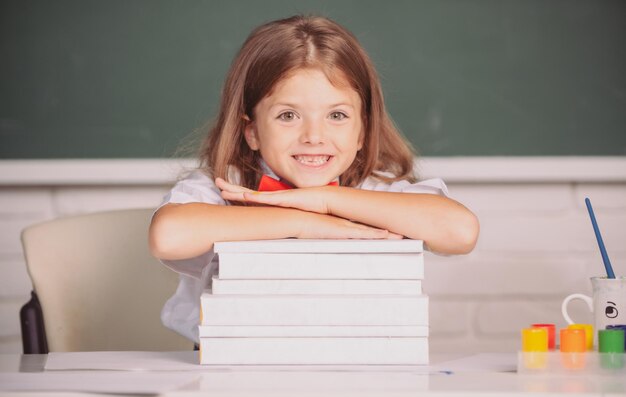 Jeune fille souriante assise au bureau et tenant les mains sur les livres dans la salle de classe de l'école