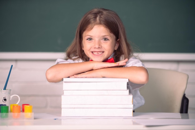 Jeune fille souriante assise au bureau et tenant les mains sur les livres dans la salle de classe Processus éducatif